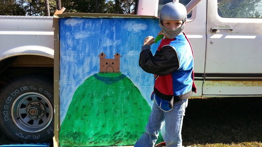 During the Roman's 2013 Global Cardboard Challenge, one of the kids  gets into costume and poses as a knight in front of the medieval-themed cardboard backdrop.  